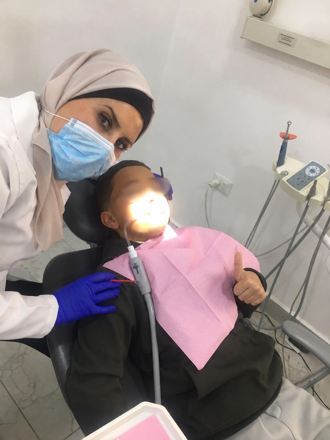 الطبيبة بجانب طفل على كرسي الأسنان، مع تغبيش منطقة العينين مراعاة للخصوصية